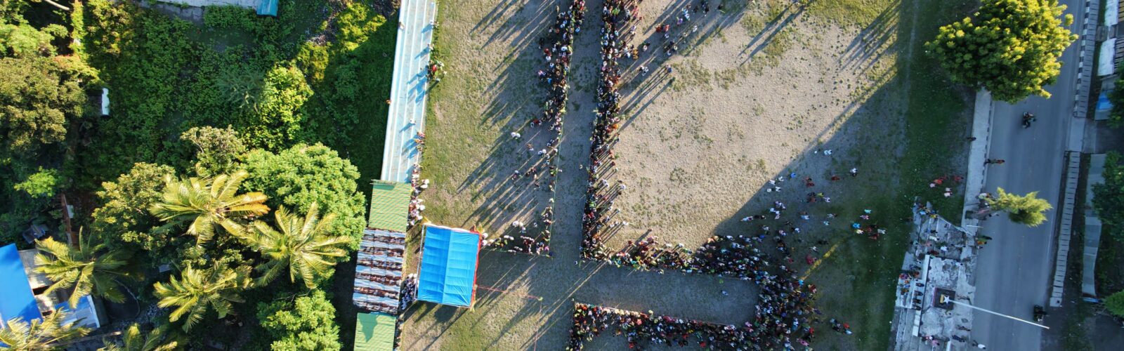 An aerial photo of people gathering to form the shape of a cross. Buildings and trees are visible.
