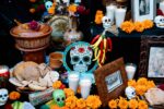 An ofrenda featuring orange and gold flowers, candles, decorated skulls, food, and other offerings for loved ones who have passed.