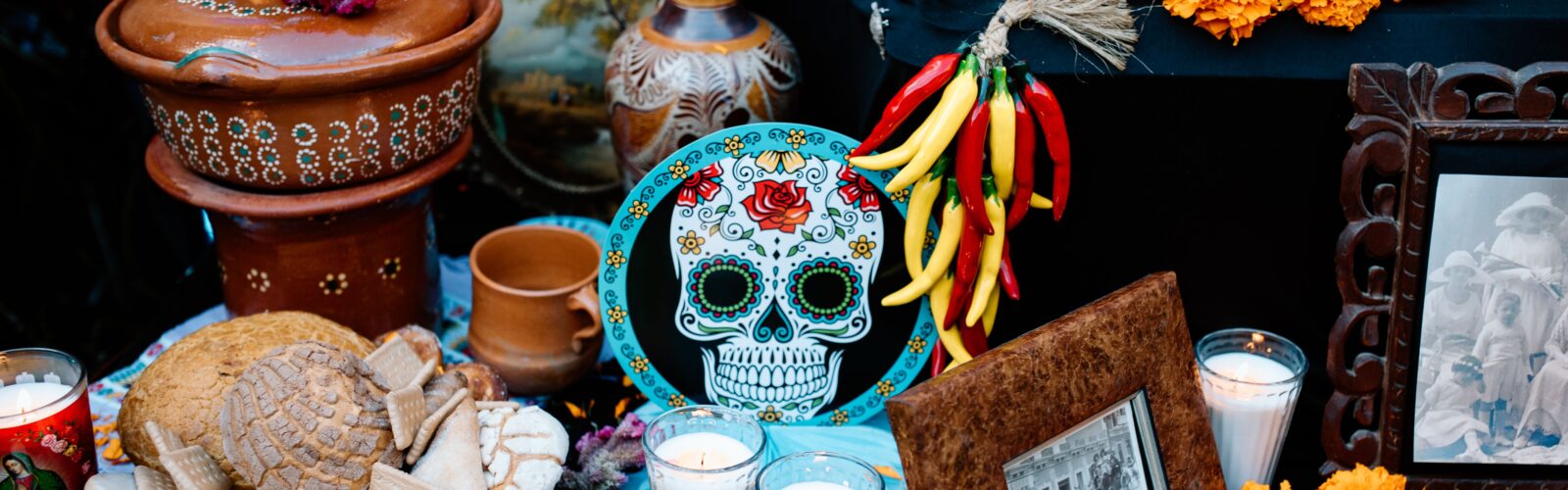 An ofrenda featuring orange and gold flowers, candles, decorated skulls, food, and other offerings for loved ones who have passed.