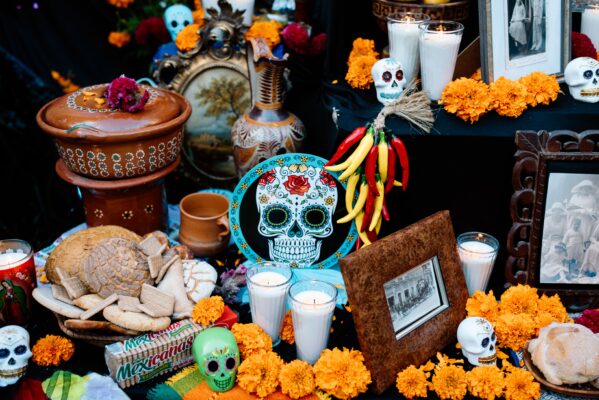 An ofrenda featuring orange and gold flowers, candles, decorated skulls, food, and other offerings for loved ones who have passed.