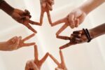 The camera looks up underneath a group of people putting their first two fingers together (connecting peace signs to make a star).